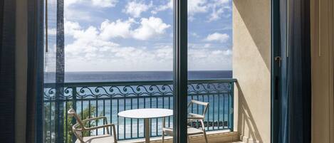 A balcony with a view of the ocean, two chairs, and a small table.