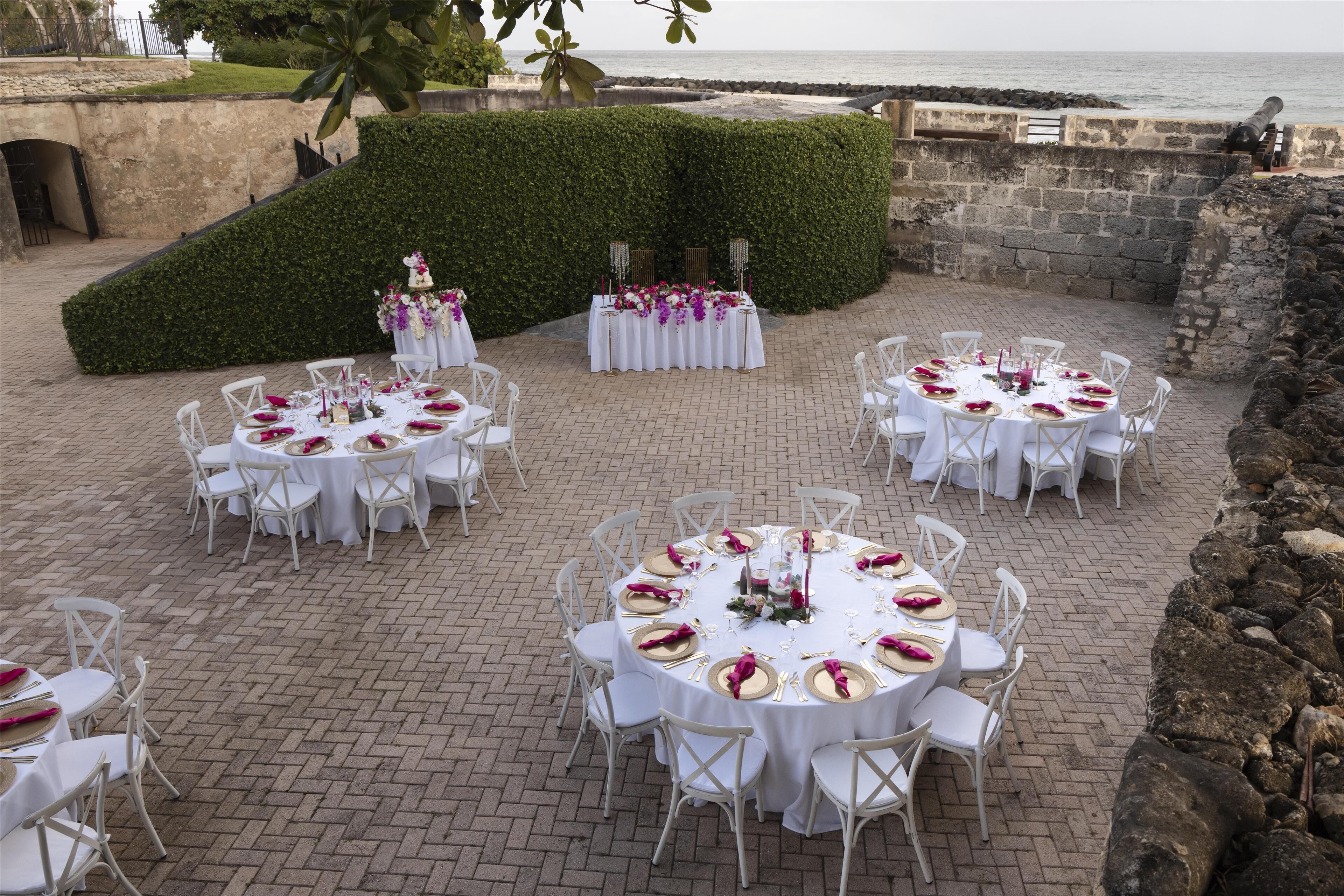 Decoración para boda al aire libre con mesas redondas, sillas blancas y adornos florales.