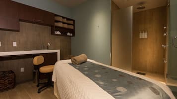 Une chambre comprenant un lit, un bureau, une chaise, un espace douche et une petite étagère avec des serviettes.