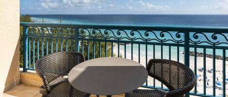 A balcony with wicker chairs and a table overlooking a beach with clear skies.