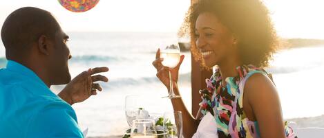 Una pareja cena en una mesa con vistas al océano, sosteniendo copas de vino.