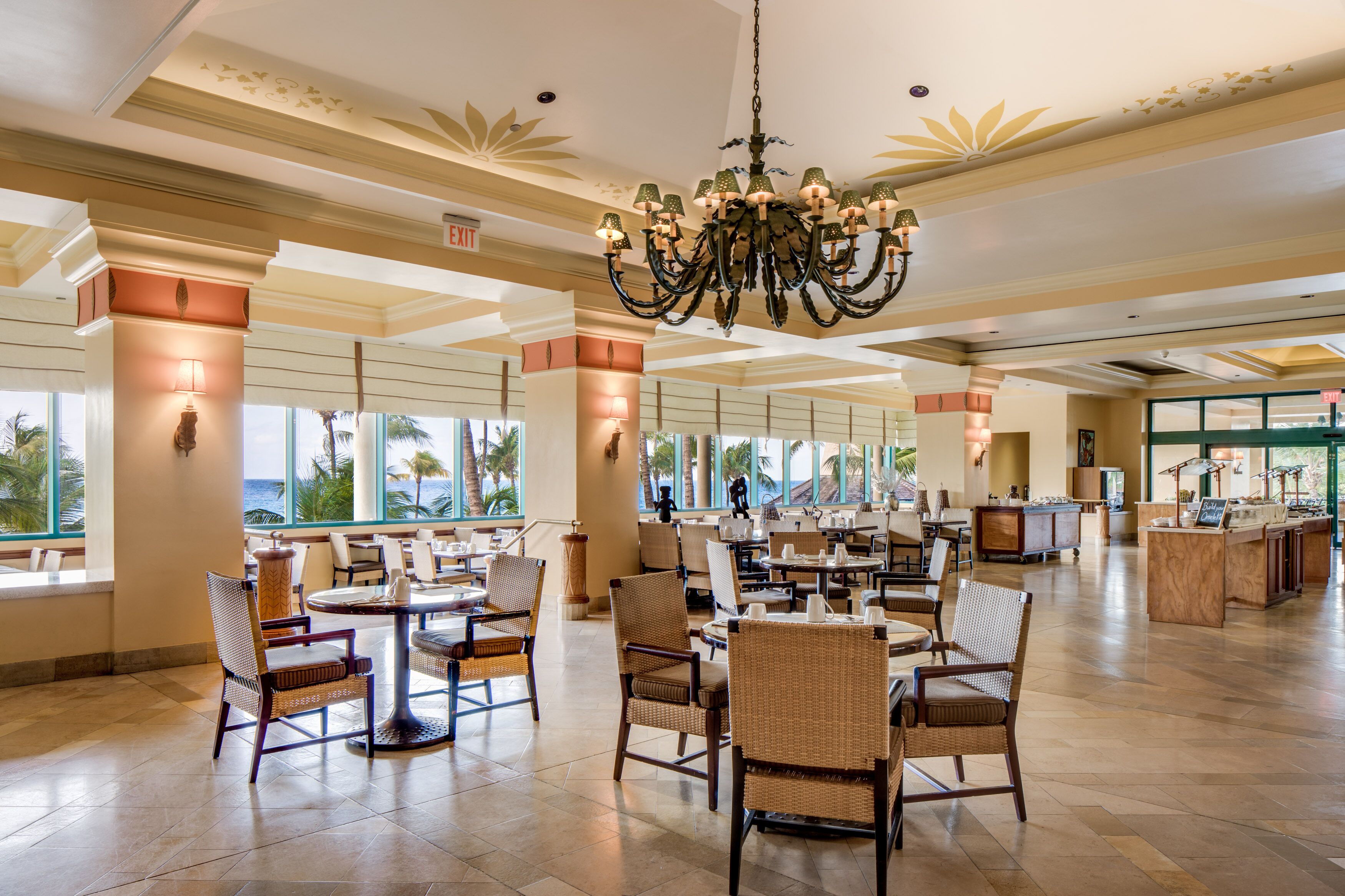 A spacious lobby with high ceilings, a grand chandelier, and large windows offering views of palm trees.