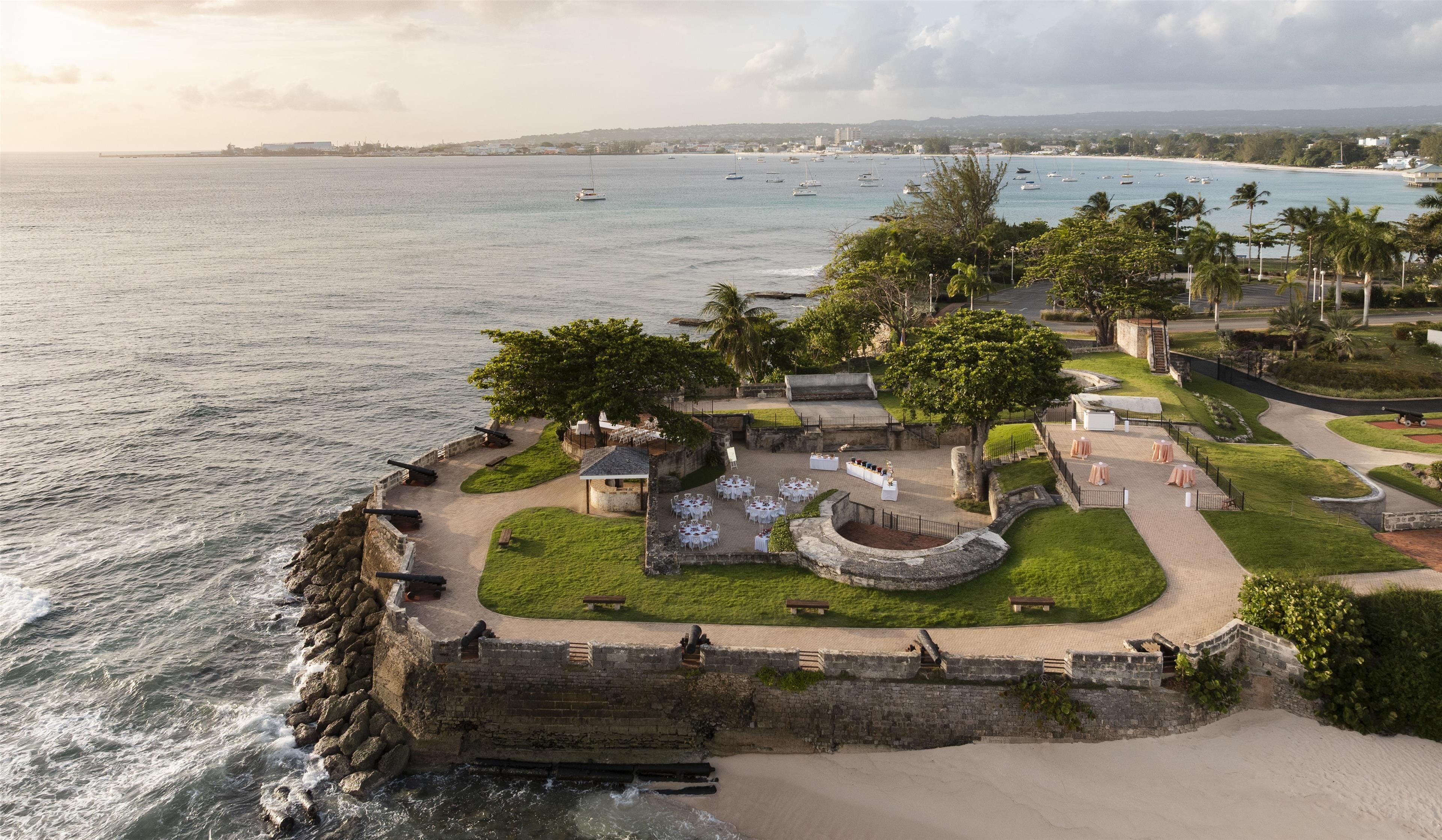 A coastal fort with a paved courtyard, seating areas, and a view of the sea.
