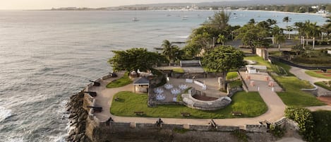 A coastal fort with a paved courtyard, seating areas, and a view of the sea.