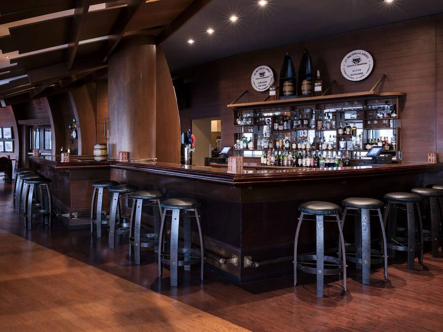 A bar area with a long counter, multiple stools, and a well-stocked bar.