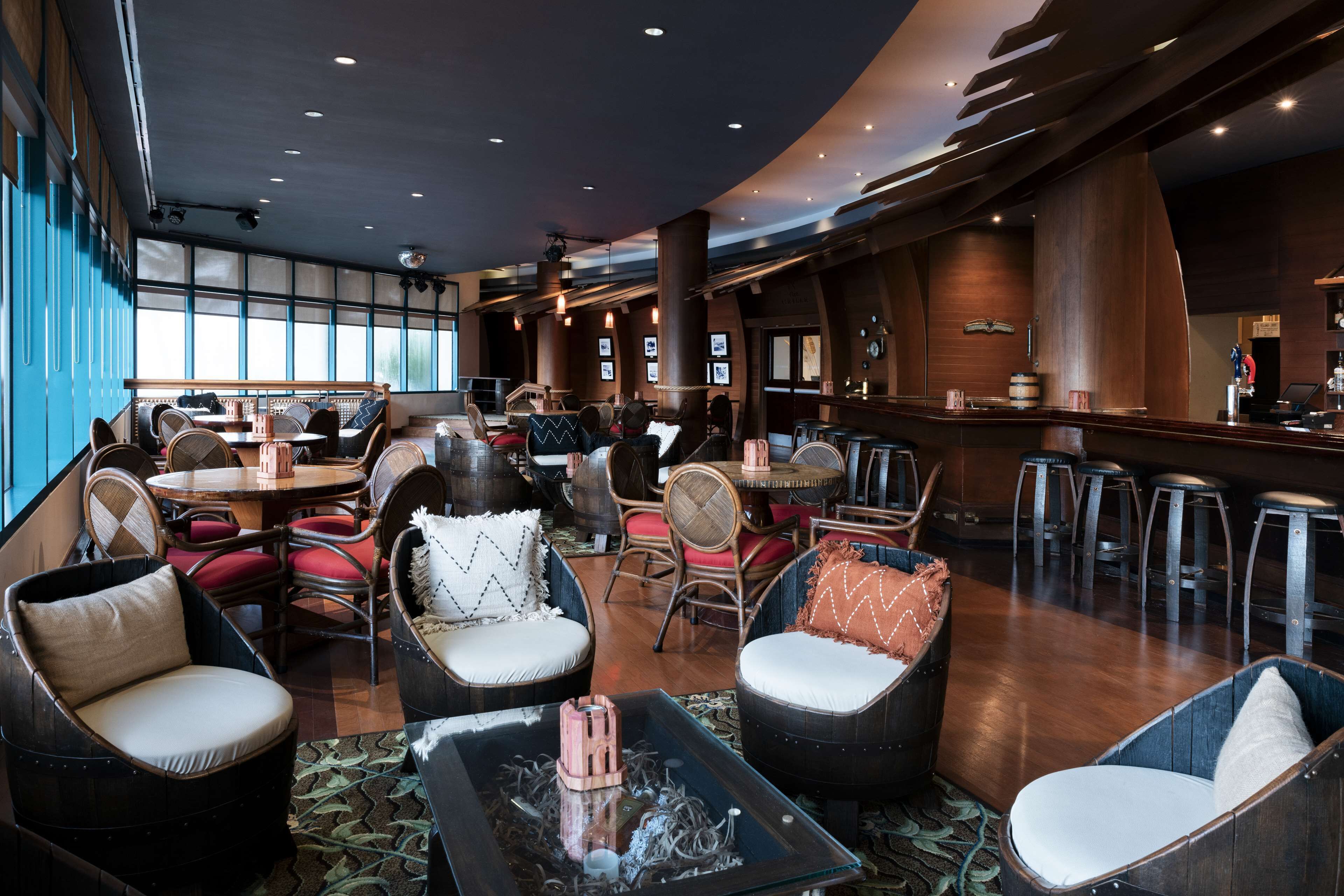 A modern lounge area with seating arrangements, a bar, and large windows providing natural light.