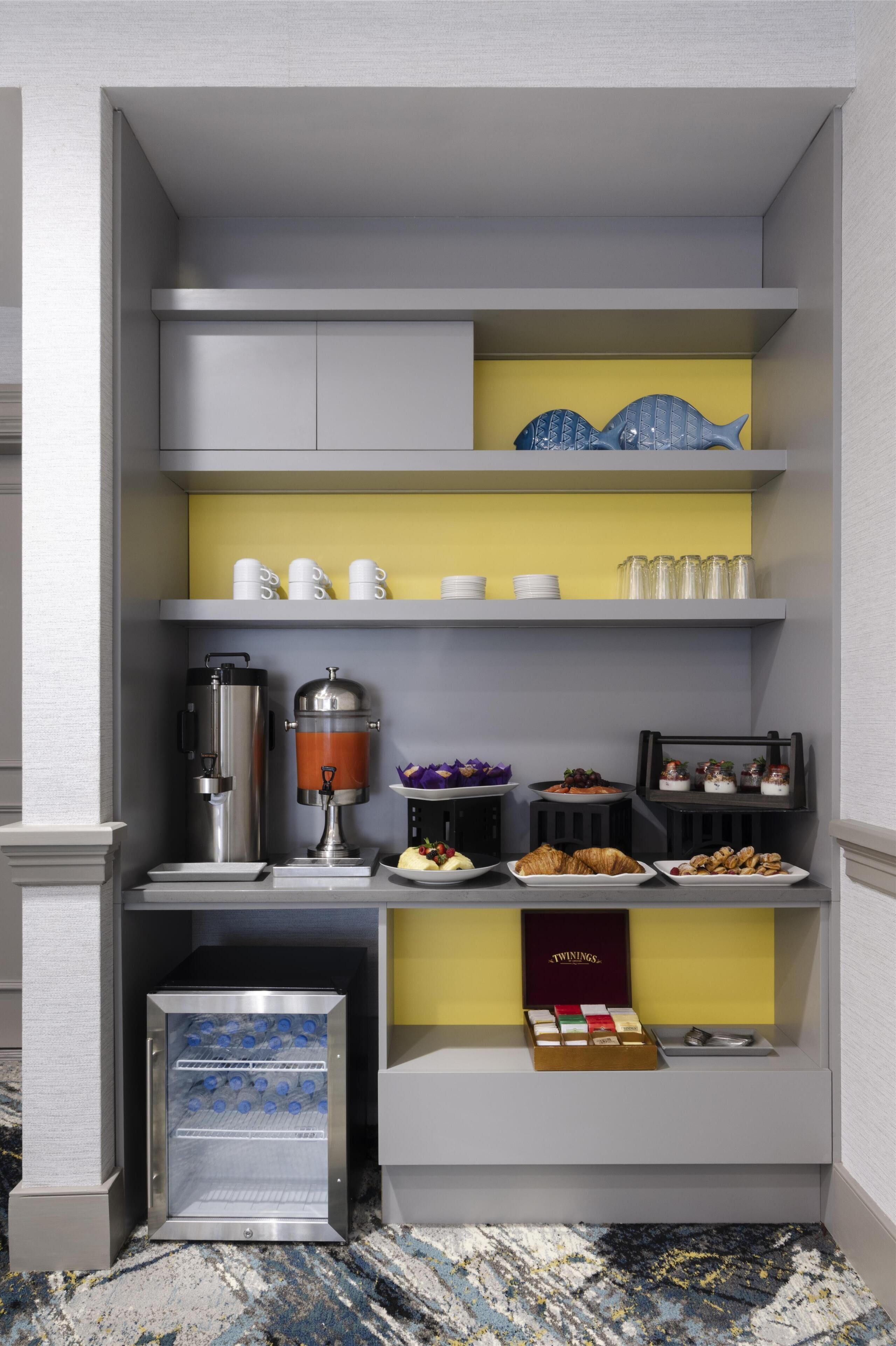 A compact breakfast bar with a coffee machine, a mini-fridge, and a variety of breakfast items.