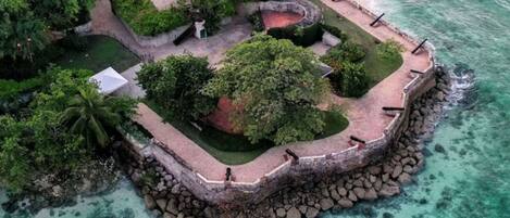 An aerial view of a coastal property with a stone wall, lush greenery, and a beach.
