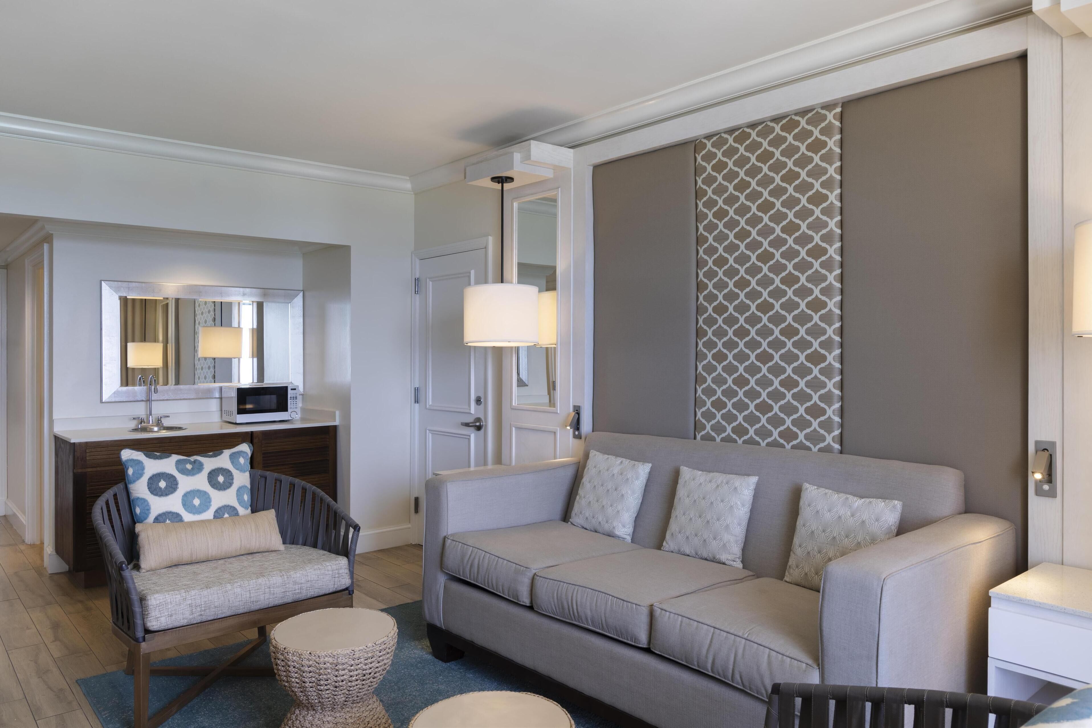 Una sala moderna con un sofá gris, un sillón estampado y una pequeña mesa redonda.