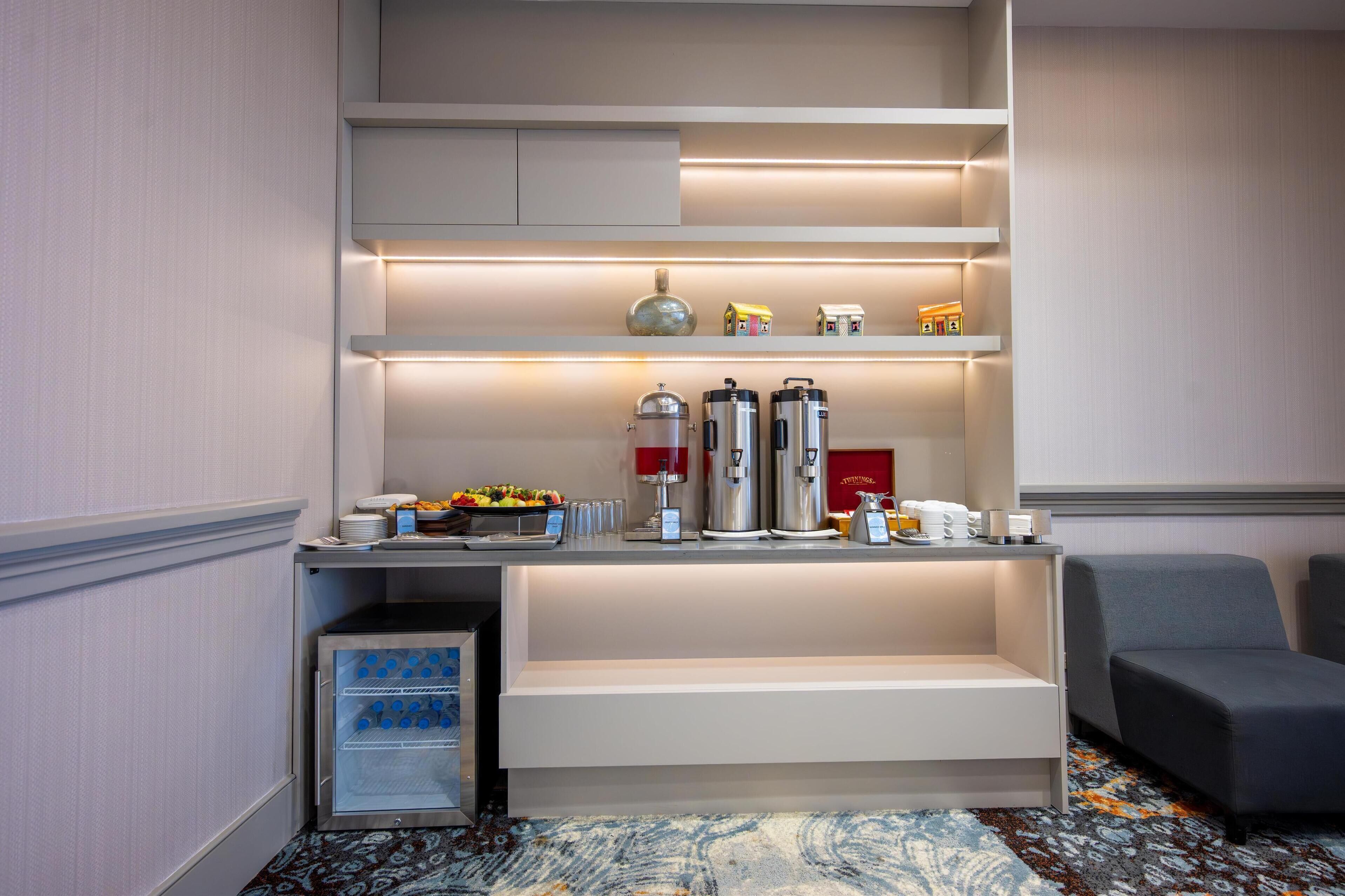 A modern hotel room with a built-in kitchenette, a seating area, and a small refrigerator.