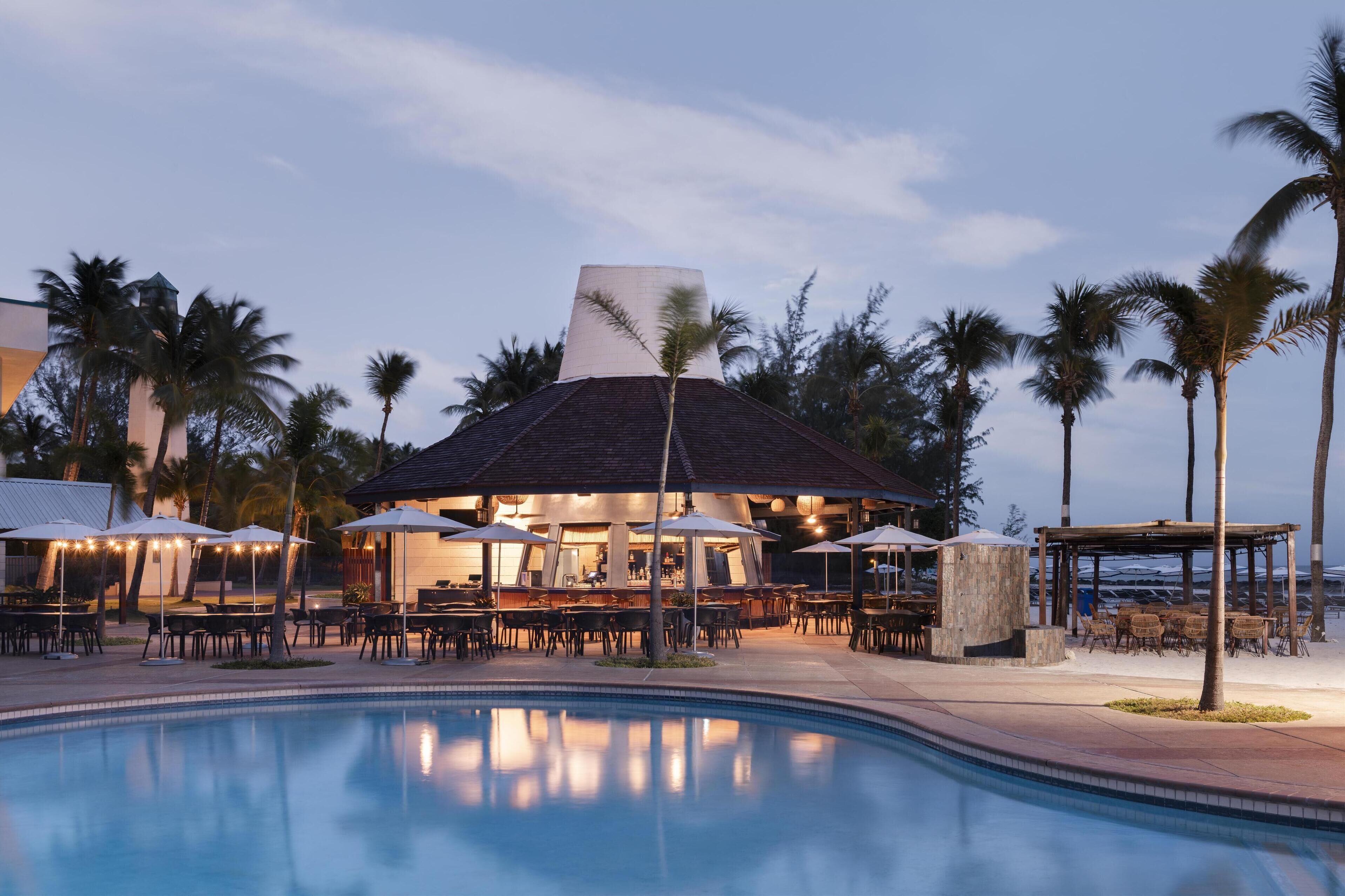 Un espace aménagé au bord de la piscine, avec des sièges extérieurs, un bar et un pavillon couvert.