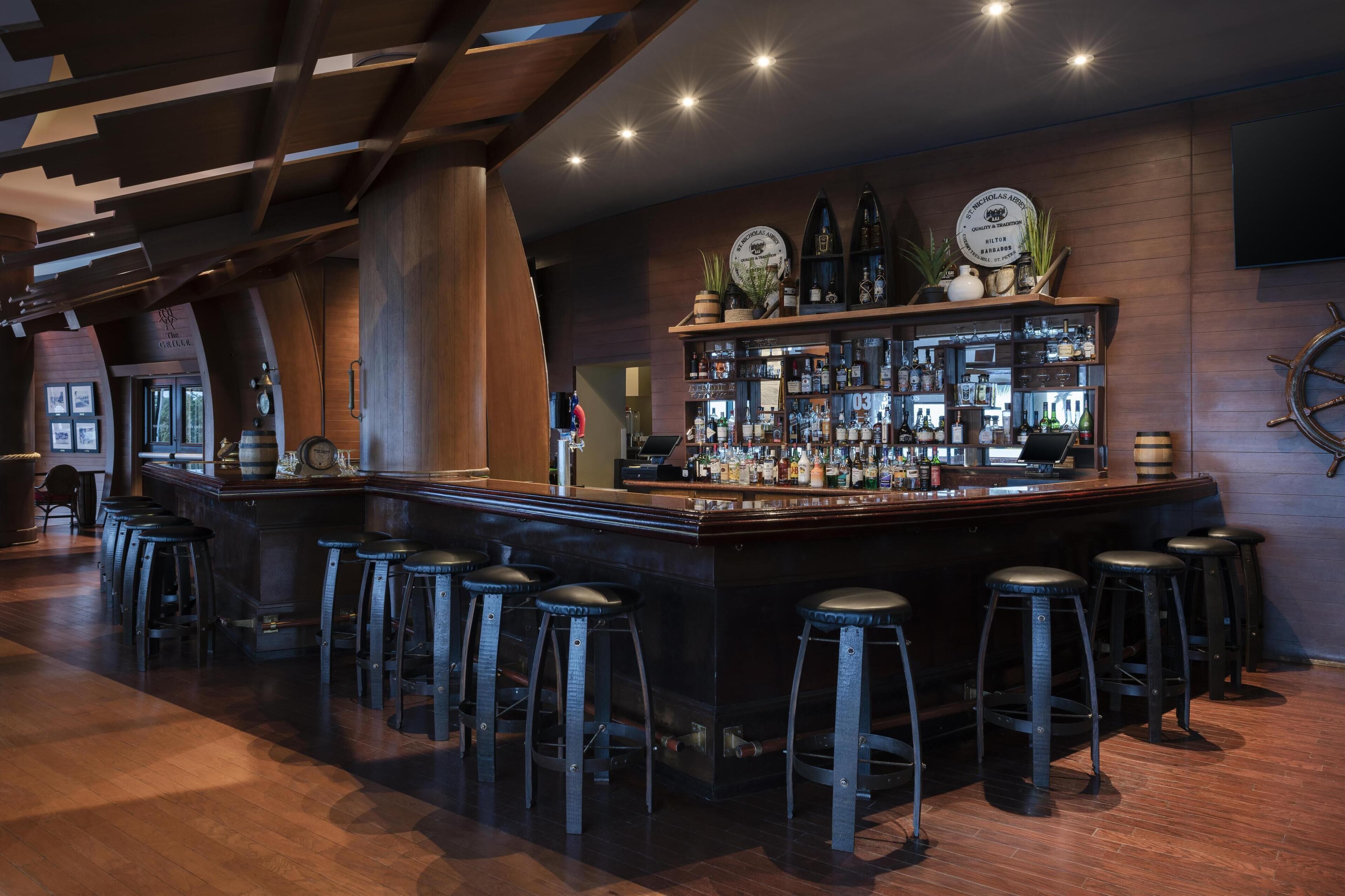 A bar area with a long counter, multiple stools, and a variety of bottles and glasses.