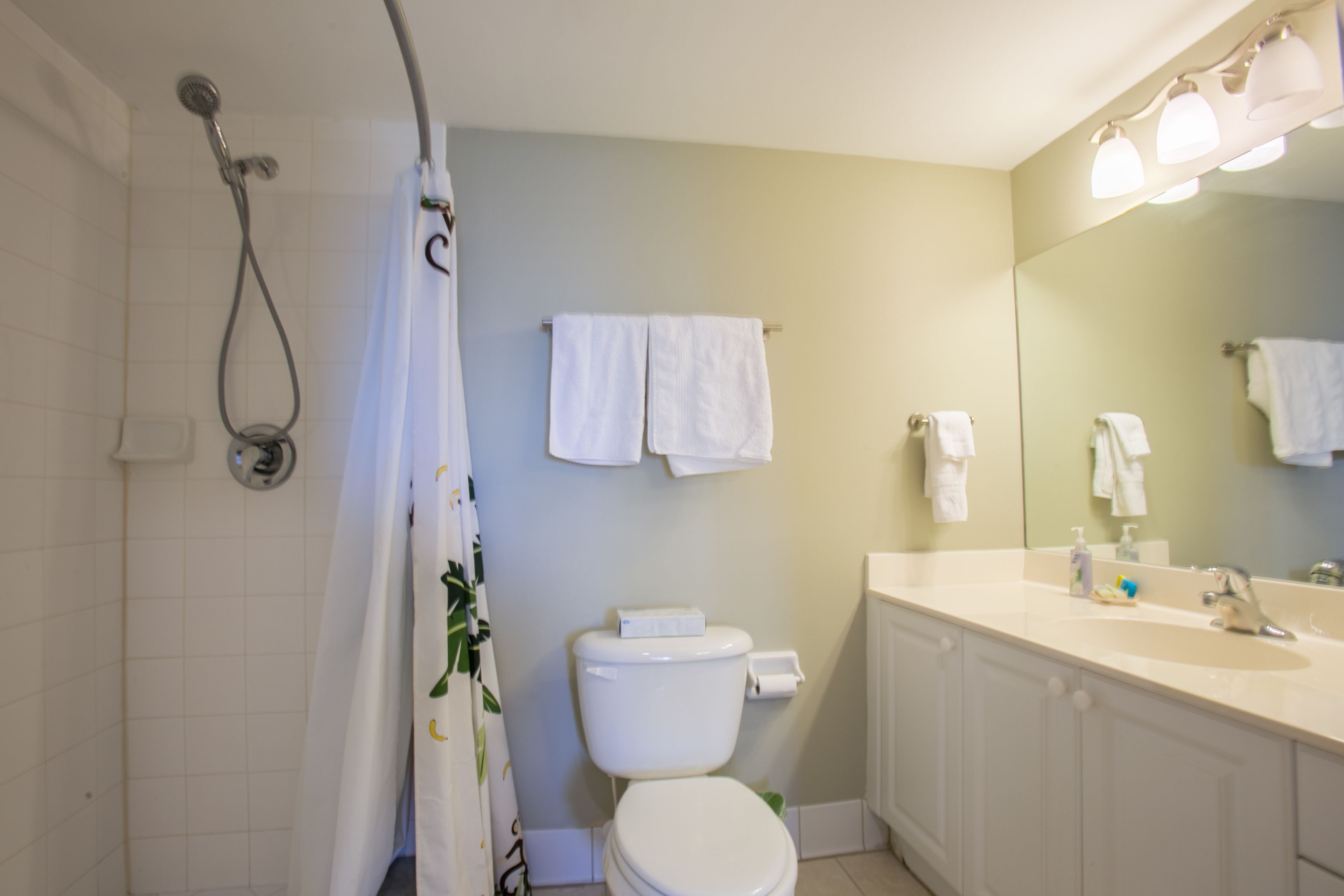 A bathroom with a shower, toilet, sink, and mirror.