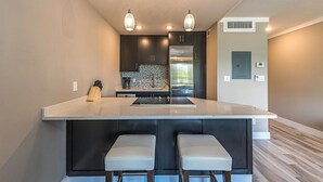 A modern kitchen with a central island, dark cabinetry, stainless steel appliances, and pendant lighting. - Marco Beach Vacation Suites (Marco Island)