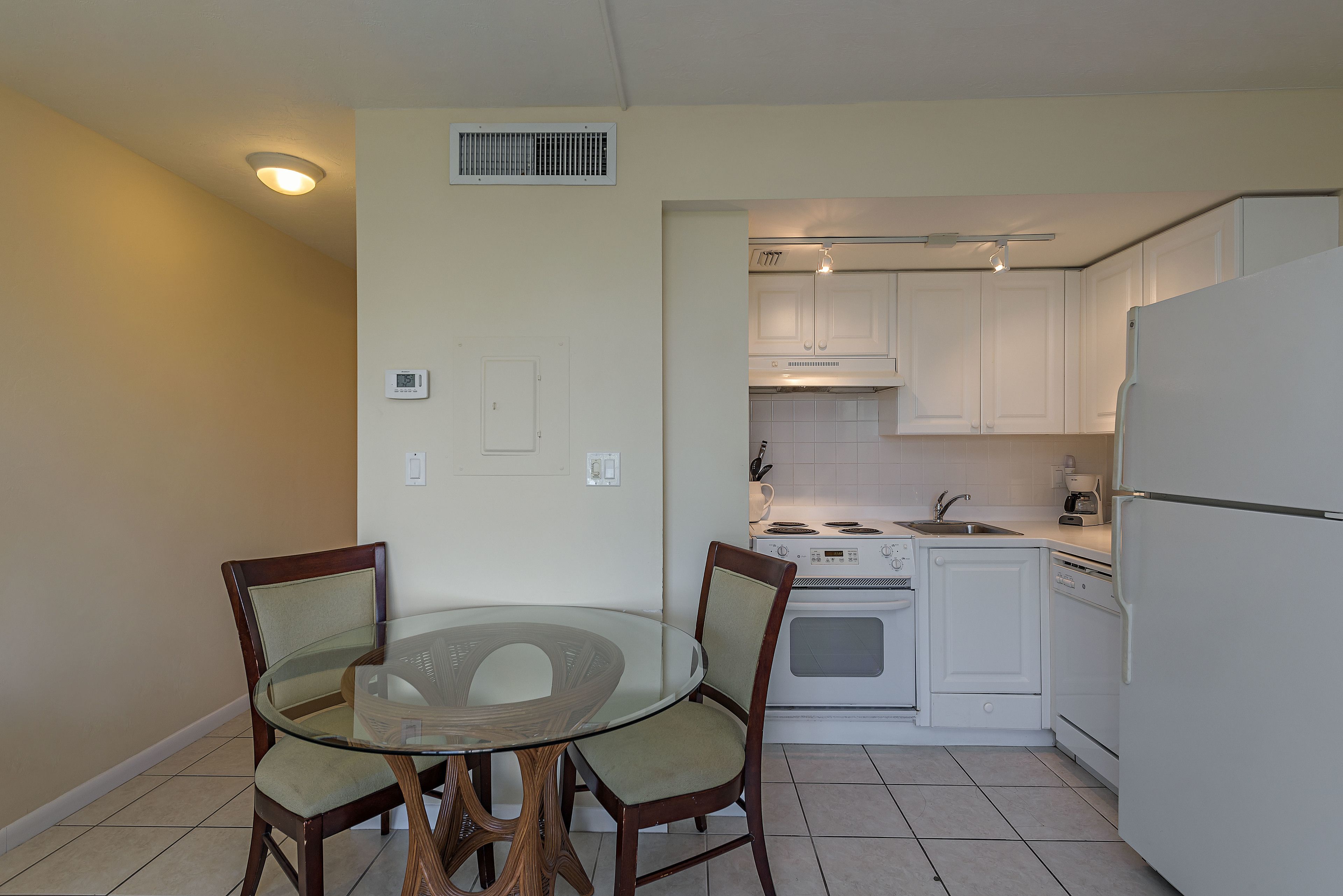 A compact kitchen with white cabinets, a stove, and a dishwasher. There is a glass table with chairs in the foreground.