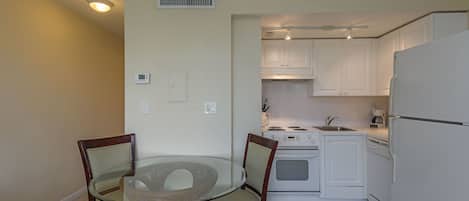 A compact kitchen with white cabinets, a stove, and a dishwasher. There is a glass table with chairs in the foreground.