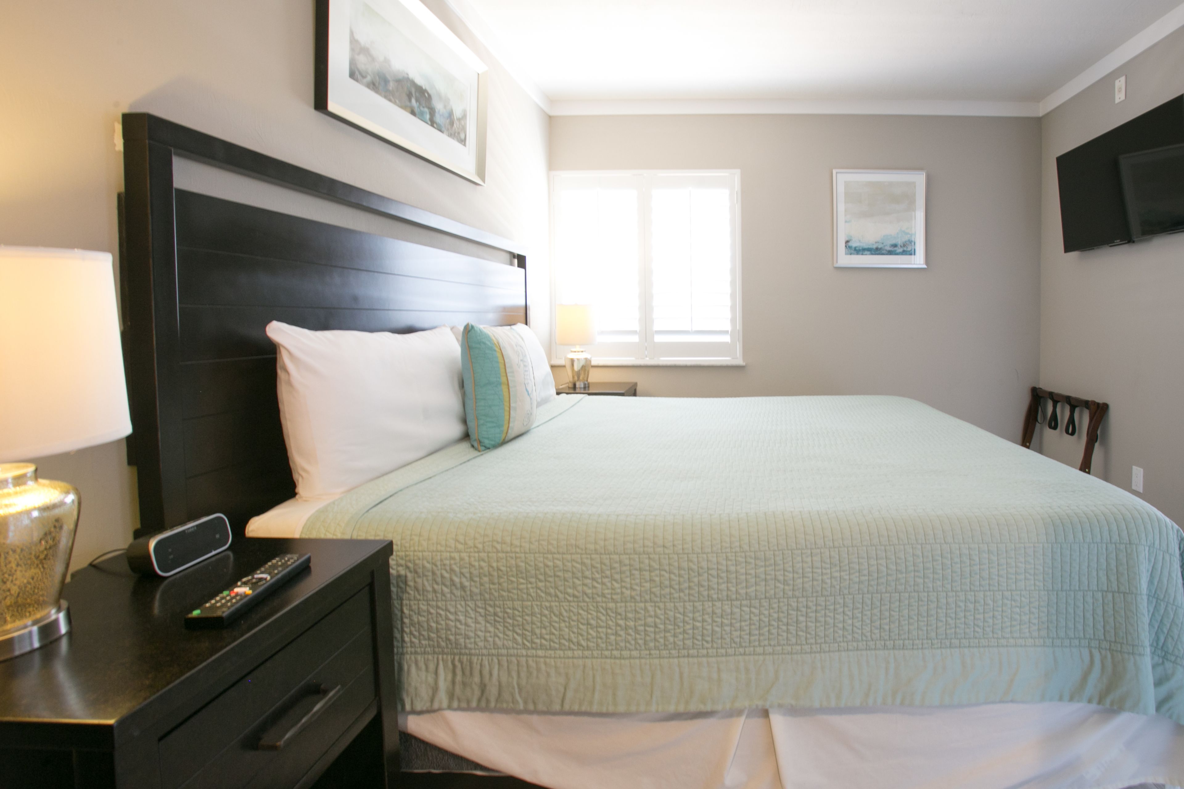A neatly made bed with a quilted cover, a bedside table with a remote control, and a lamp.