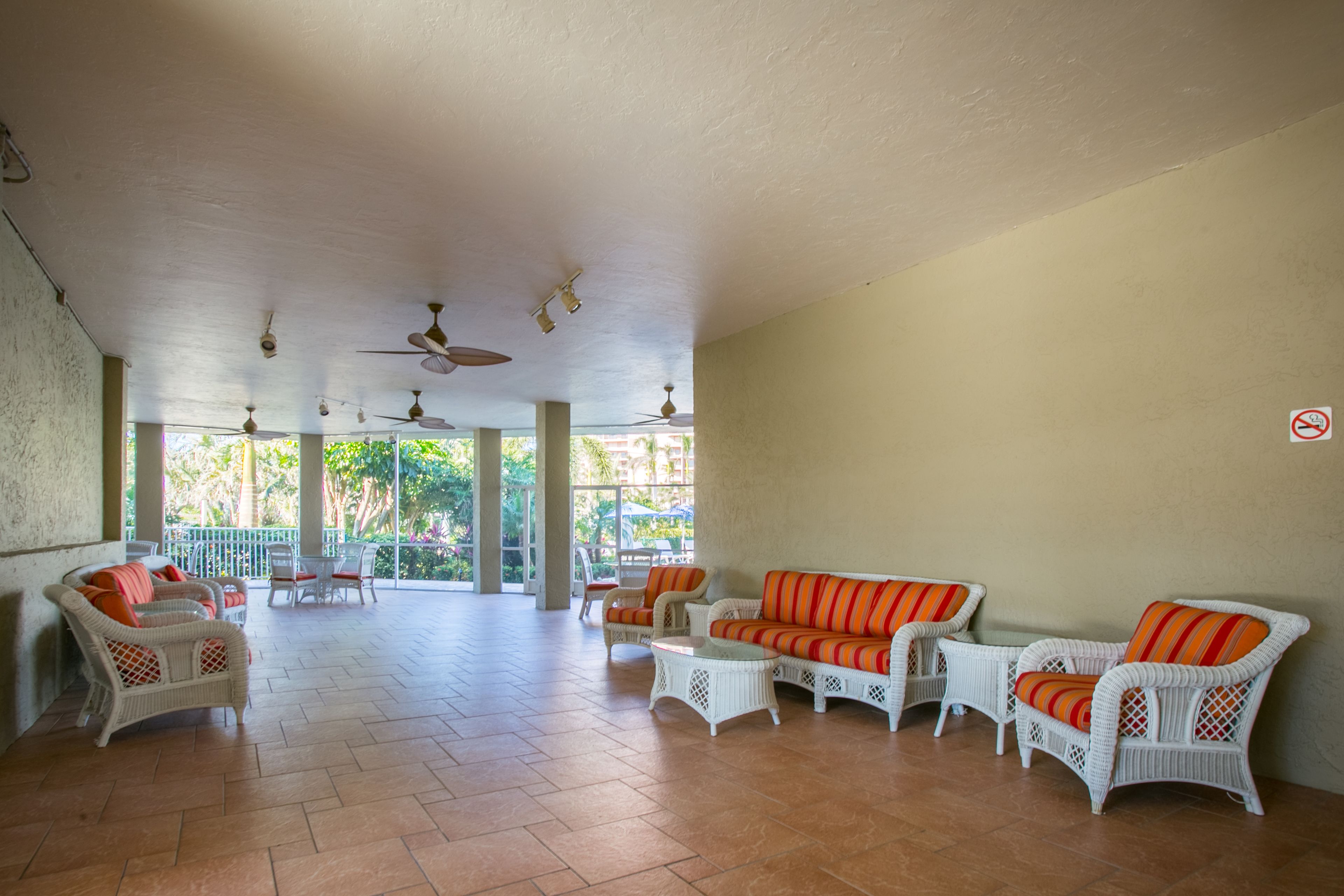 A spacious indoor area with wicker furniture, ceiling fans, and large windows.
