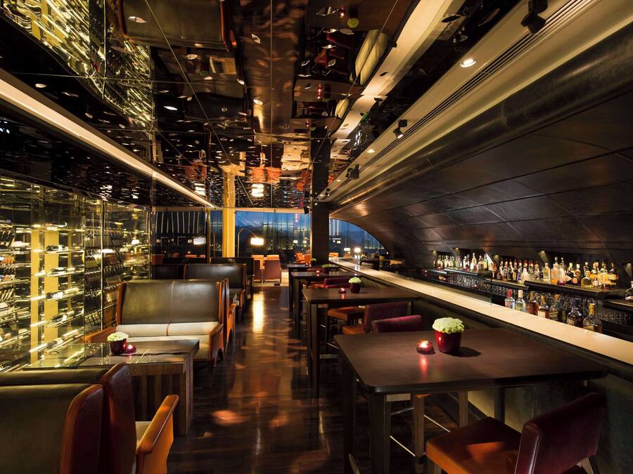 A modern bar area with seating, a bar counter, and a view of the cityscape.