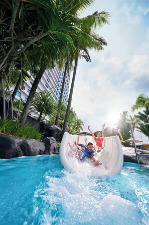A water slide in a pool area with palm trees and a building in the background.