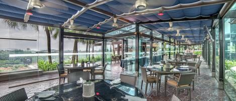A rooftop restaurant with glass walls, outdoor seating, and ceiling fans.