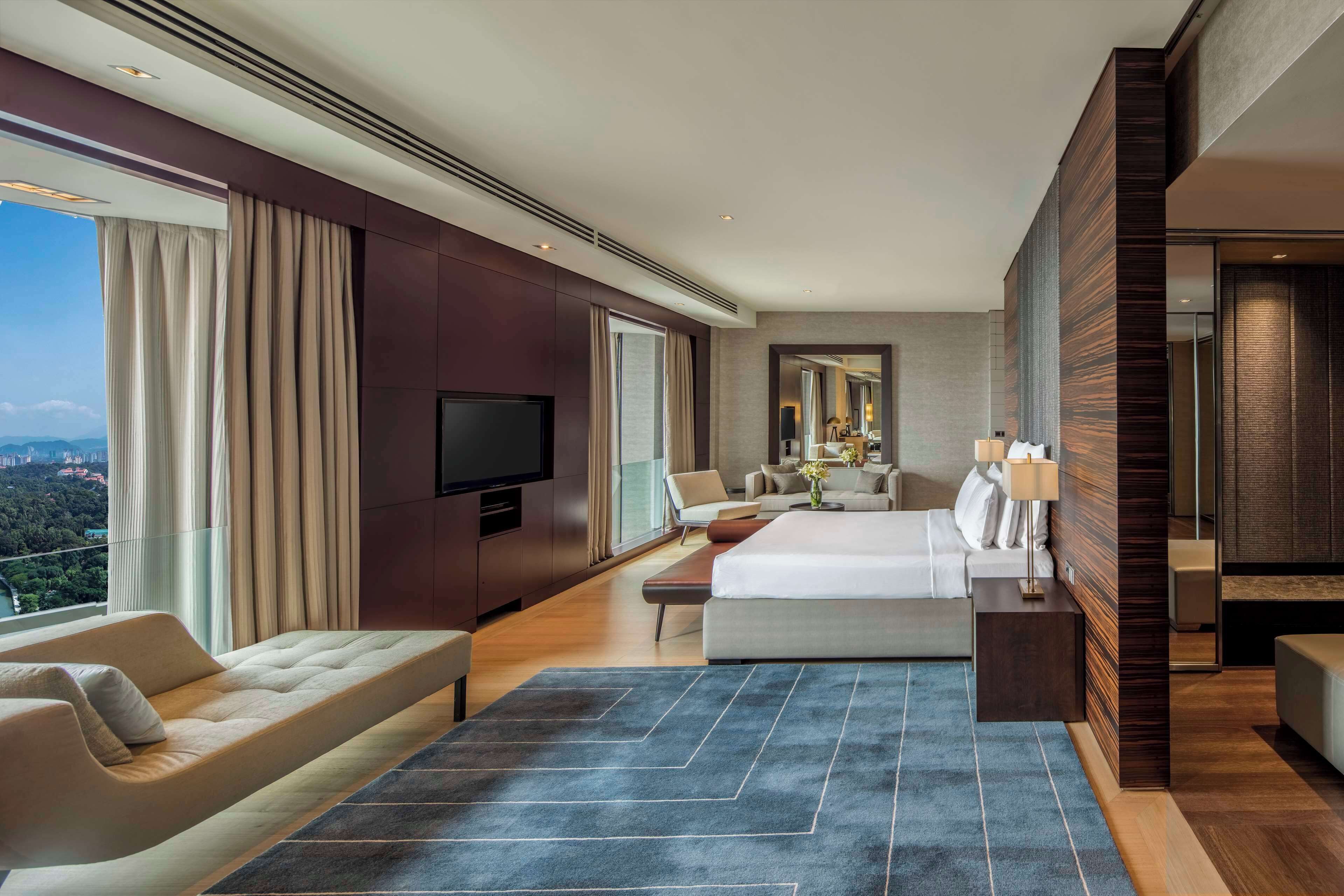 A modern hotel room with a large bed, a sofa, a TV, and a view of the city.