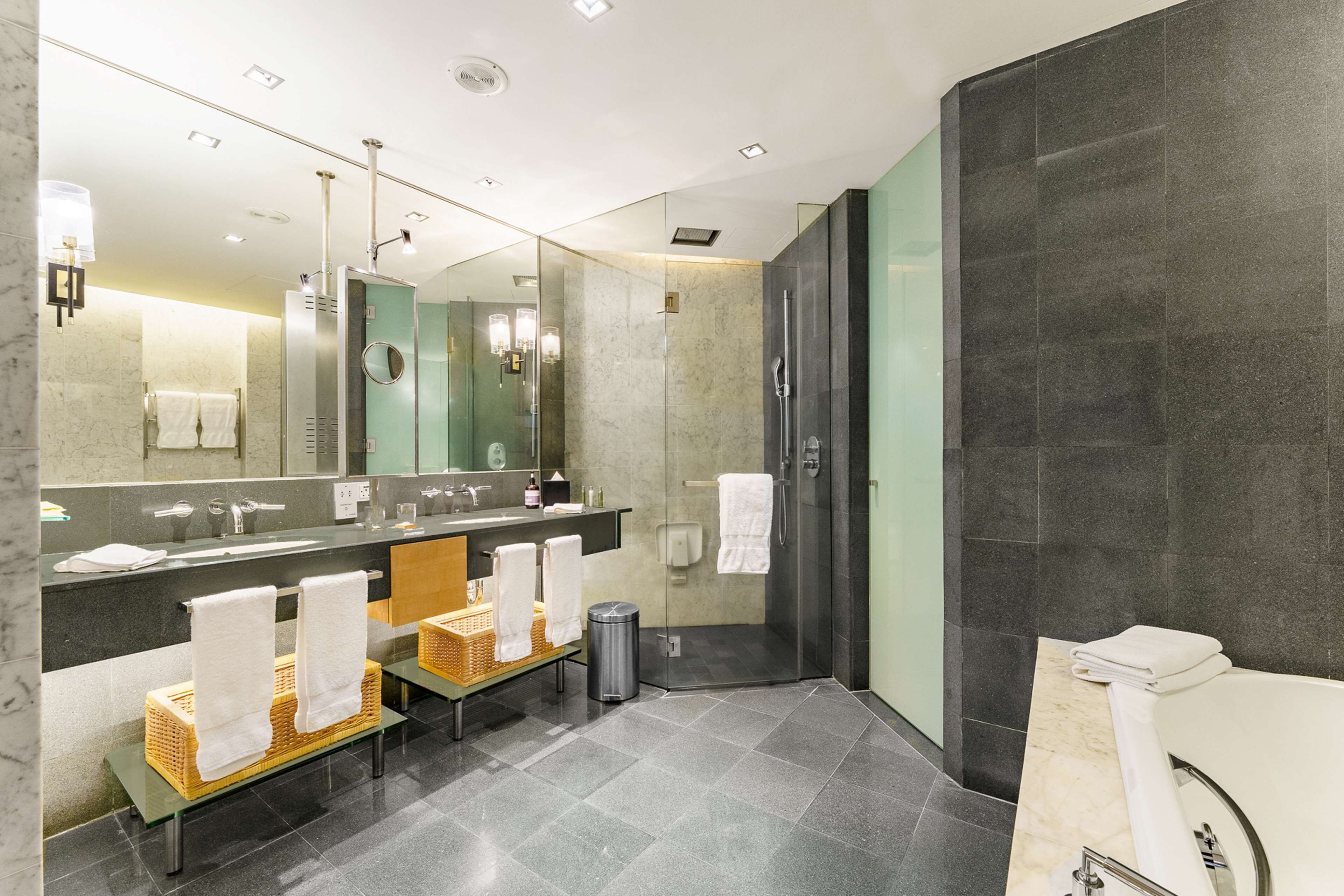A modern bathroom with a large mirror, two sinks, a shower, and a toilet.
