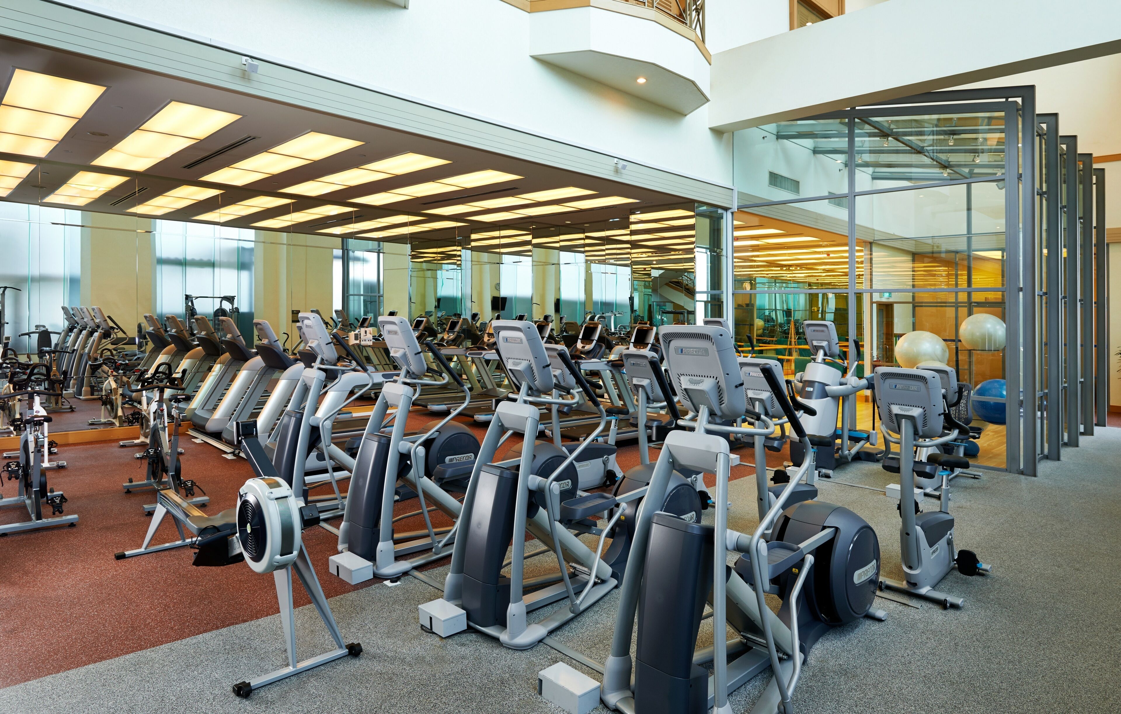 A gym with various exercise machines, a mirrored wall, and a glass door leading to another area.