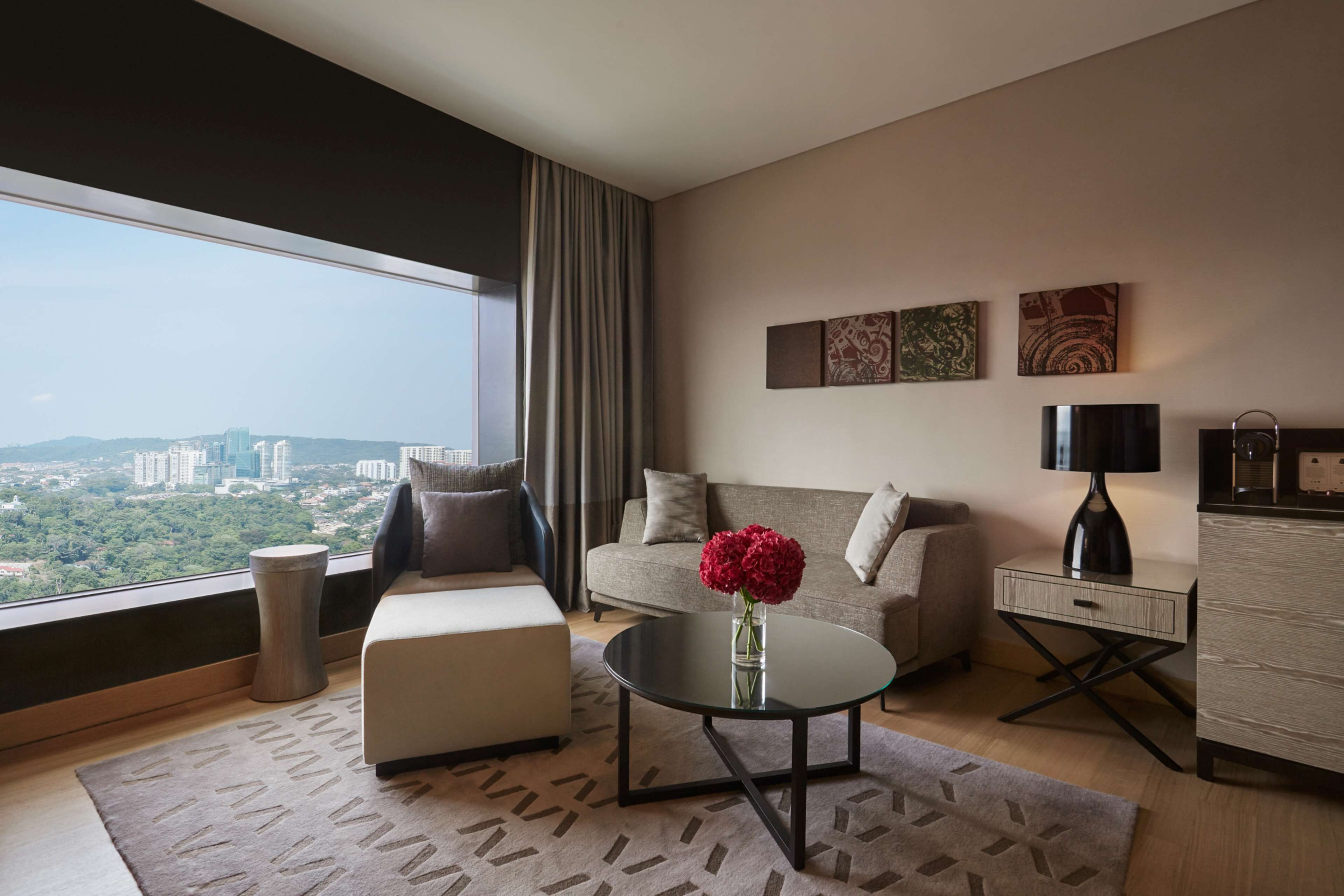 A modern living room with a sofa, a coffee table with a vase of flowers, a desk, and a view of a cityscape.