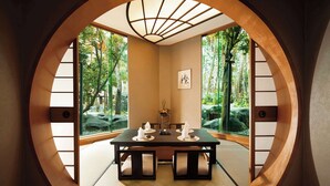 A traditional Japanese room with tatami flooring, a low table with cushions, and a view of a forest through a circular window. - Hilton Kuala Lumpur (Kuala Lumpur)
