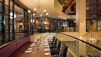 A modern dining area with a long table set for a meal, surrounded by glass railings and a curved bench.