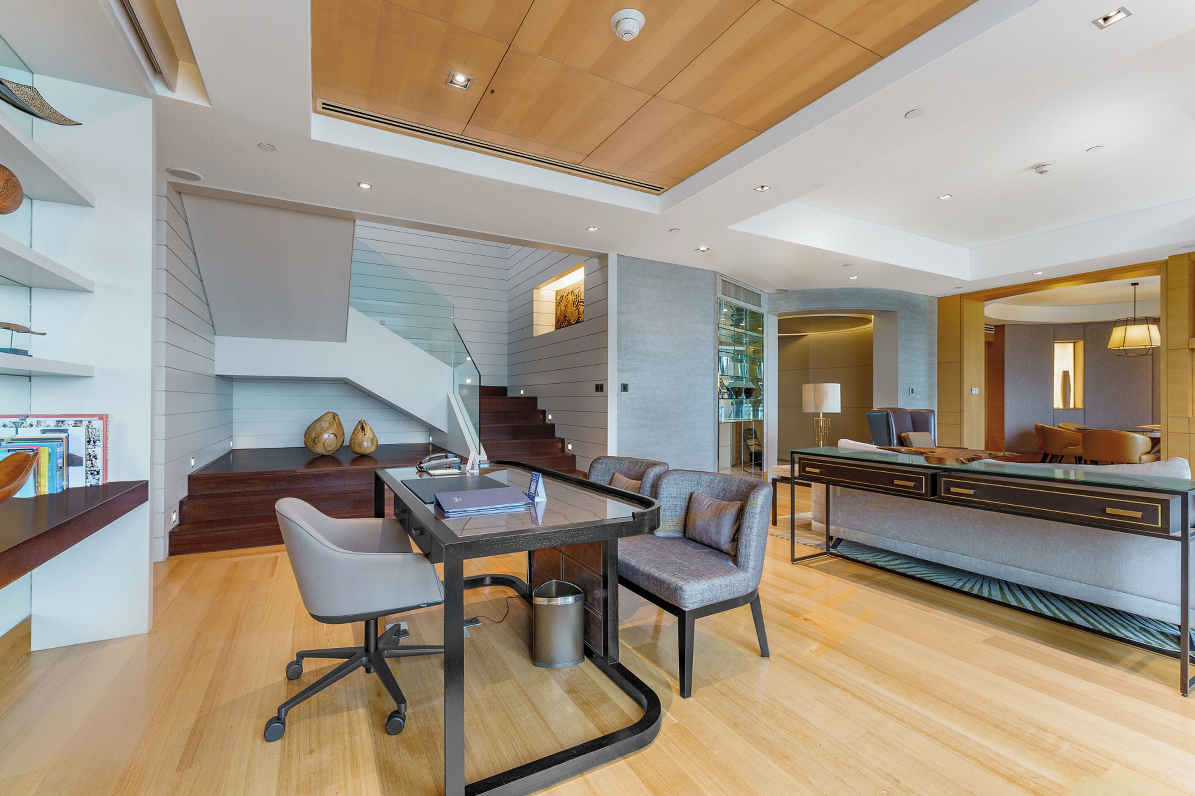 A modern living room with a glass table, a sofa, and a staircase.