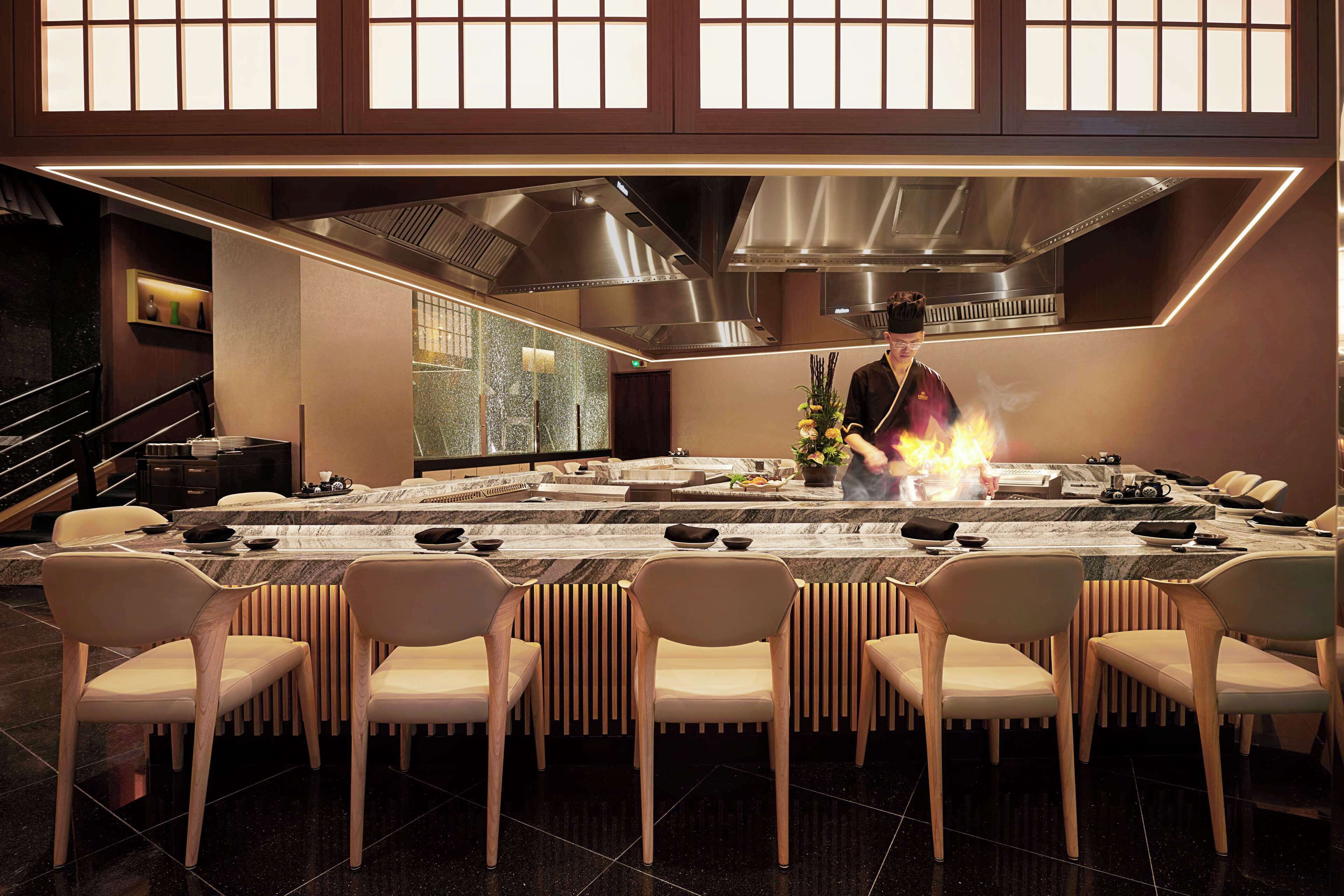 Un comedor moderno con una mesa larga, varias sillas y una estación de cocina central con llamas.