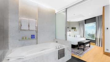 Un baño de hotel moderno con una bañera grande, un estante de vidrio con artículos de tocador y un espejo amplio.