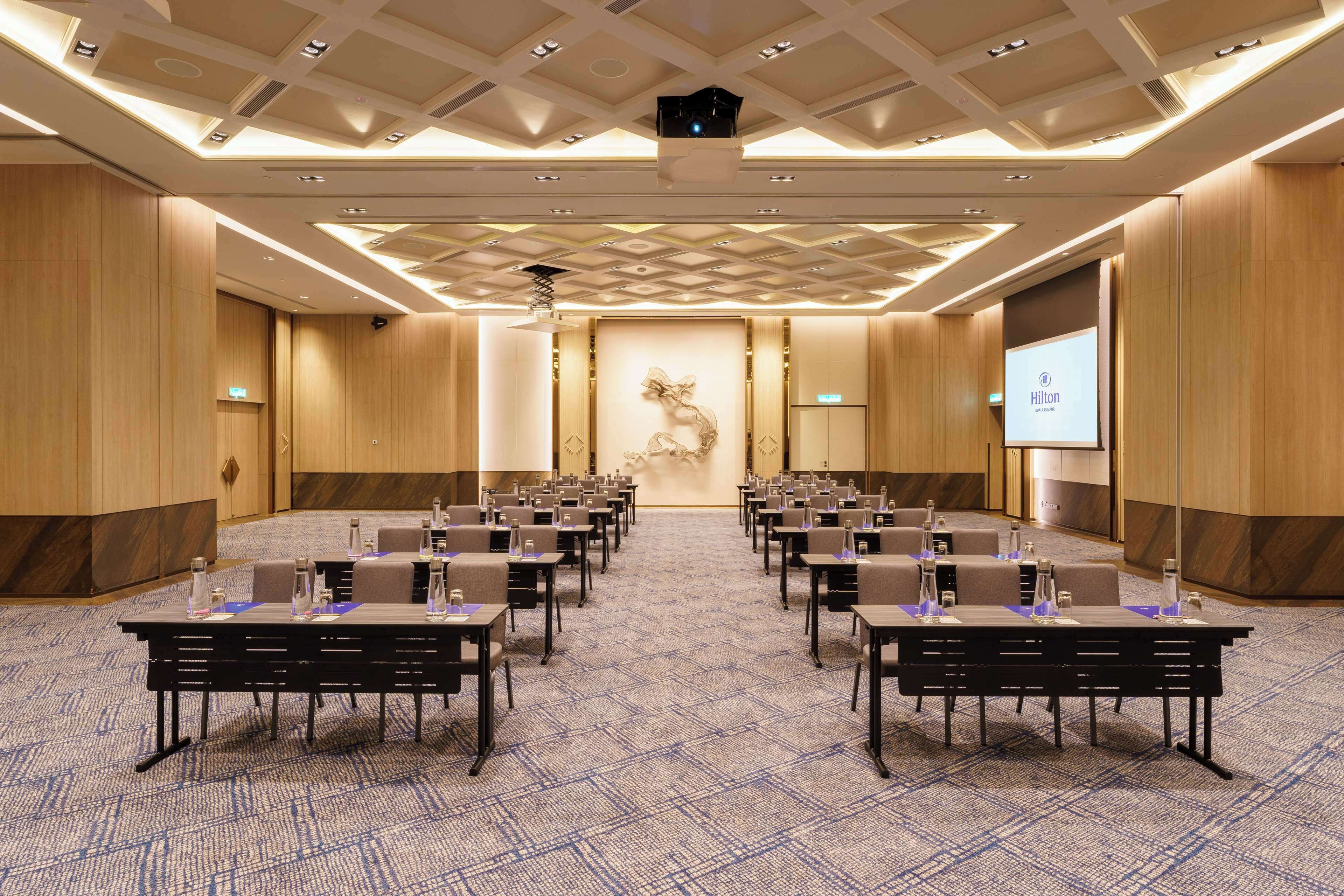 A conference room with rows of tables and chairs, a large screen, and a projector at the front.