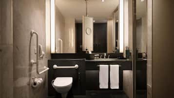 A modern bathroom with a toilet, bidet, and shower. It features a large mirror, dark tiles, and a glass shower enclosure.