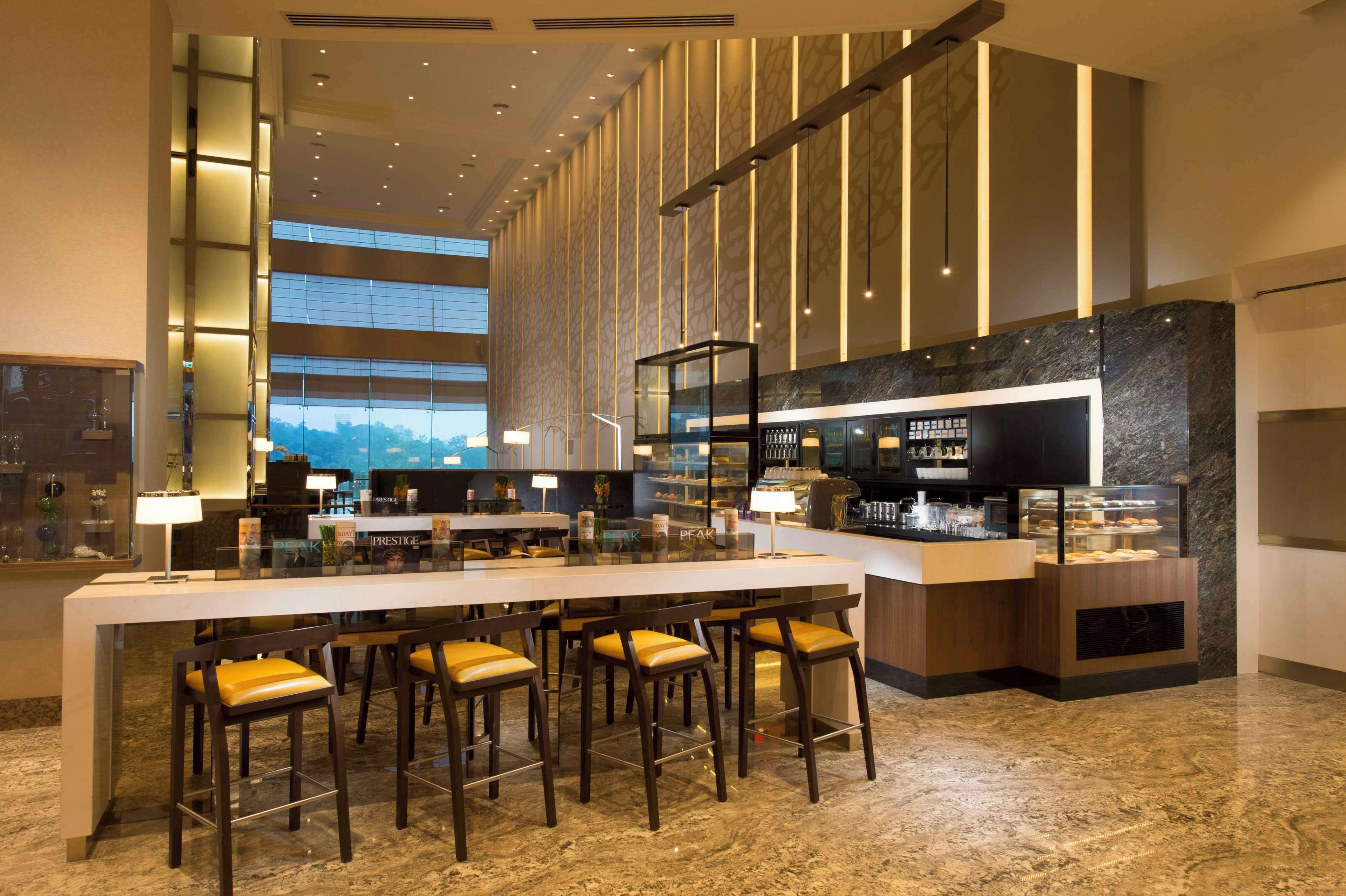 Eine moderne Hotelhalle mit einer langen Rezeption, mehreren Barhocker und einer Vitrine mit Gebäck.