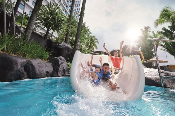 A water slide at a poolside area with palm trees and a building in the background. - Hilton Kuala Lumpur (Kuala Lumpur)