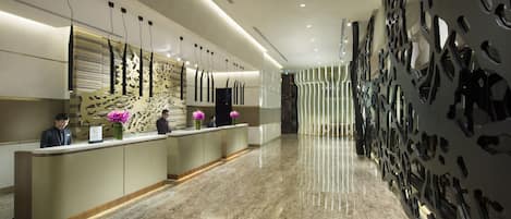 Una moderna zona de recepción con suelo de mármol, mostrador de recepción y paneles decorativos en la pared.