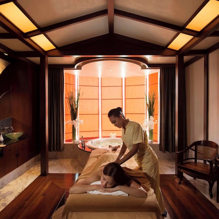 A massage room with a wooden floor, a massage table, a massage chair, and a window with curtains.