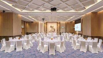 A large conference room with multiple round tables, white chairs, and a carpeted floor.