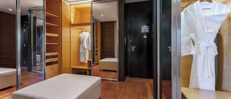 A modern hotel room with a glass-enclosed walk-in closet, a white bed, and a robe hanging on a rack.