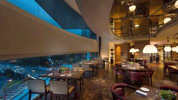 A restaurant with tables set for dining, large windows overlooking a cityscape, and a modern interior design.
