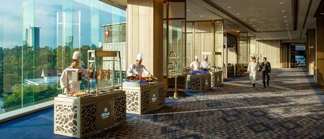 A hotel lobby with a view of the cityscape, a buffet area with chefs, and a patterned carpet.