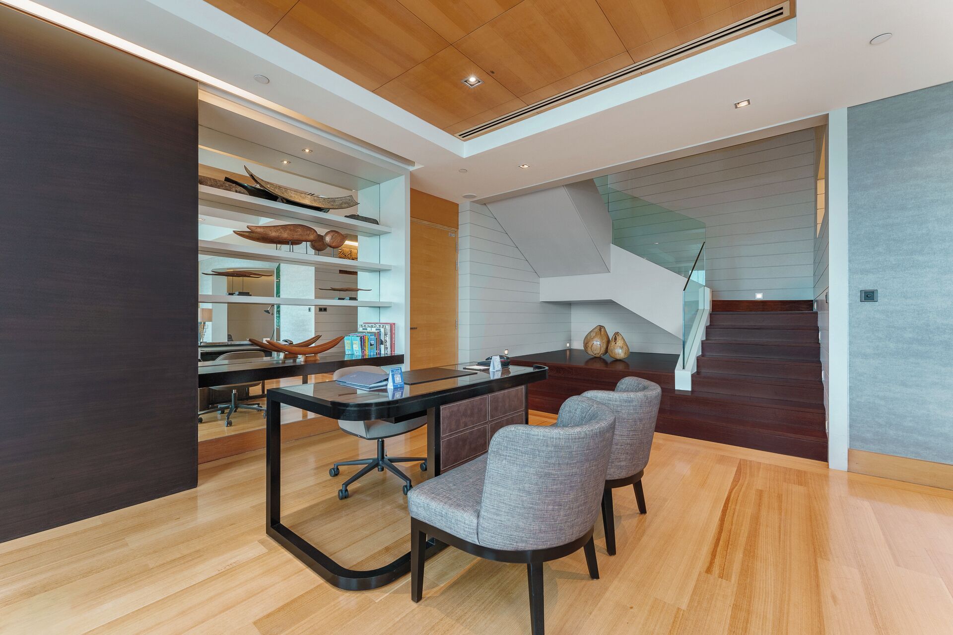 A modern interior with a wooden ceiling, a glass staircase, and a dining area with a black table and grey chairs.