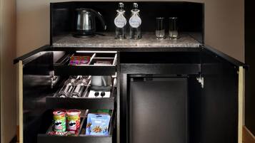 A compact kitchen with a built-in refrigerator, a coffee maker, two bottles of water, and a kettle.
