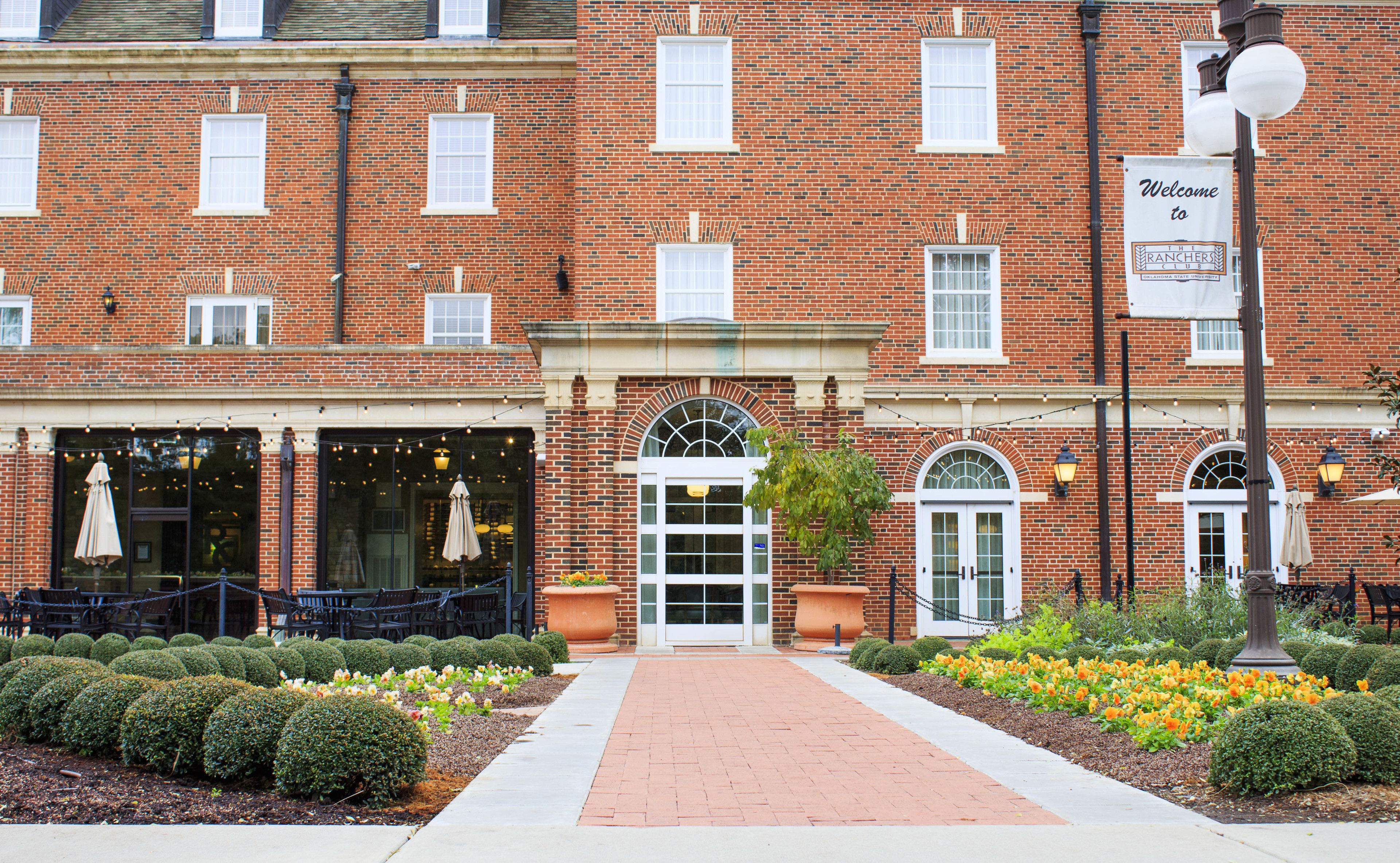 A brick building with a central entrance, outdoor seating, and a sign welcoming visitors.