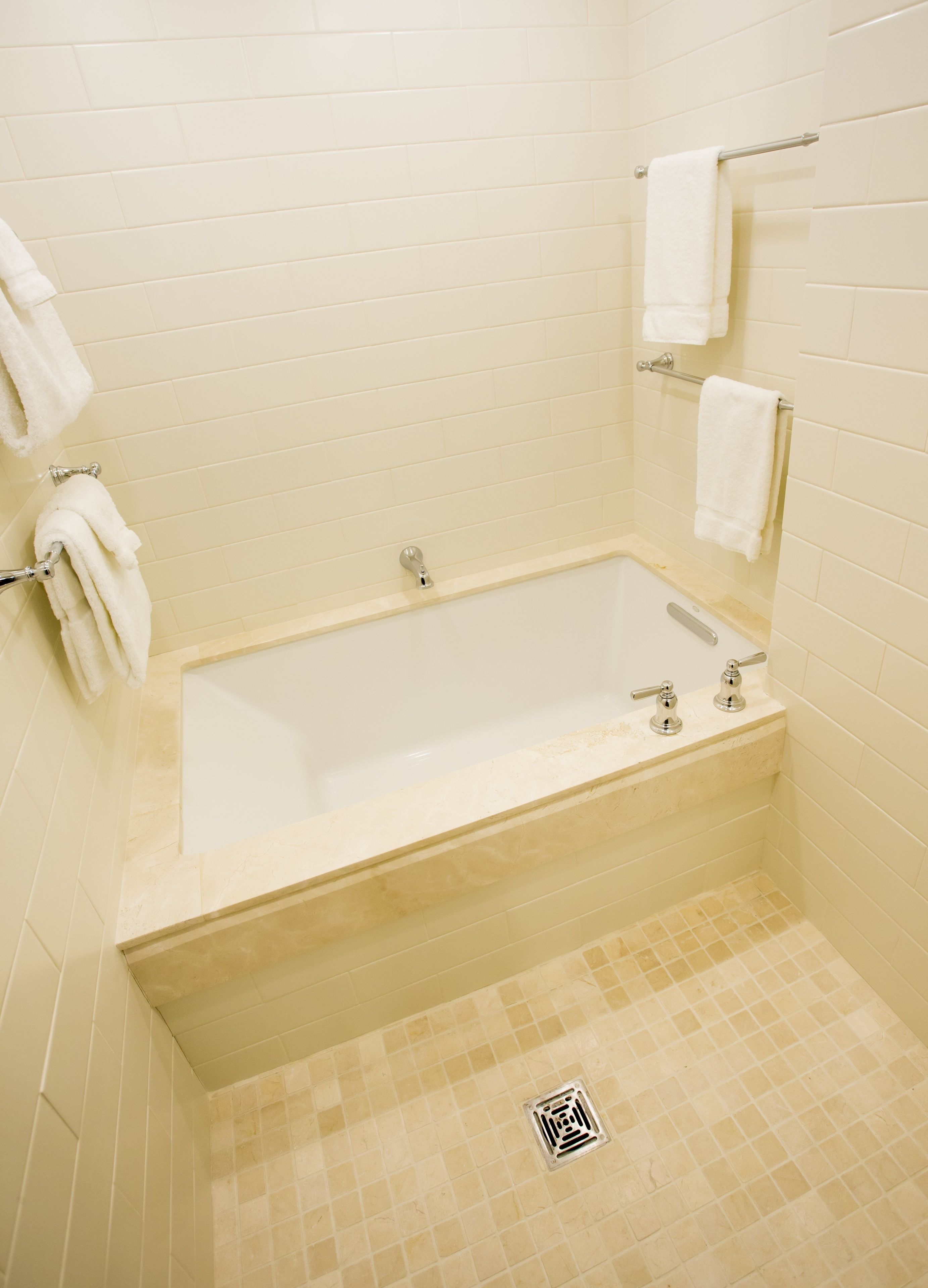 A bathroom with a bathtub, tiled walls, and a shower drain.