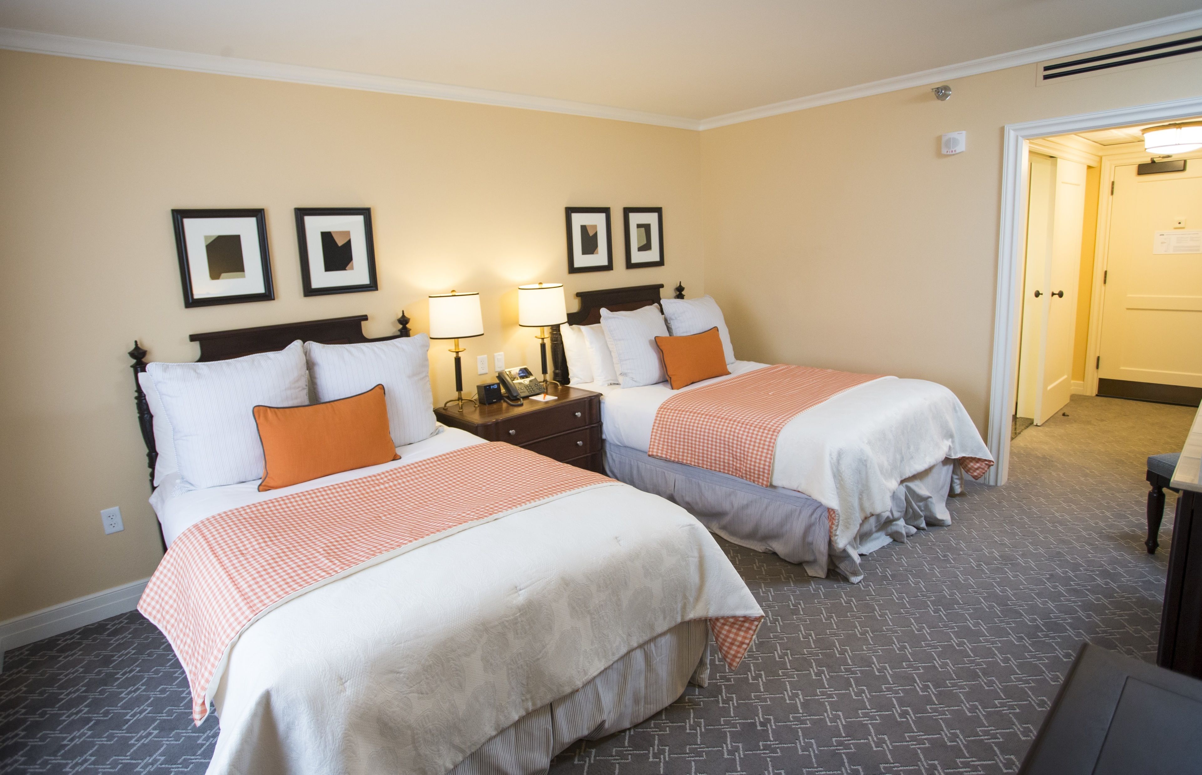 A hotel room with two beds, each with a checkered bedspread and pillows, a nightstand with a lamp, and framed pictures on the wall.