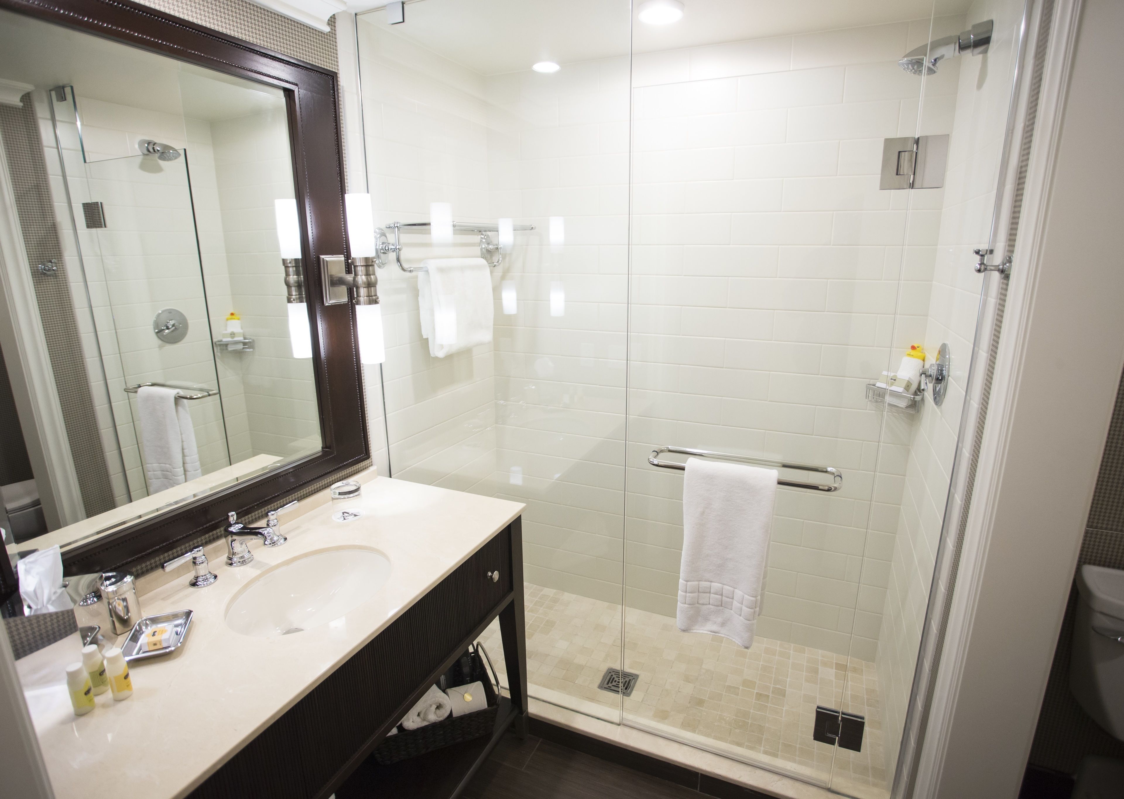 A modern bathroom with a glass-enclosed shower, a large mirror, and a vanity with a sink and toiletries.